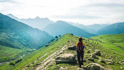 Eine Frau mit Rucksack und Trekkingstöcken beim Trekking vor Bergkulisse in Kaschmir 