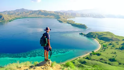 Wanderer auf einem Hügel über grünen Wiesen und dem Meer auf den Komodo Inseln in Indonesien