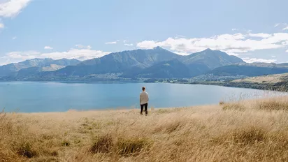 Frau blickt auf einen See und Berge in Queenstown, Neuseeland