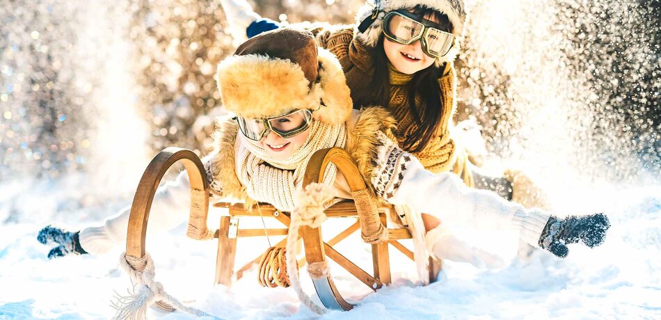 Zwei Kinder sitzen auf einem Schlitten in einer verschneiten Winterlandschaft
