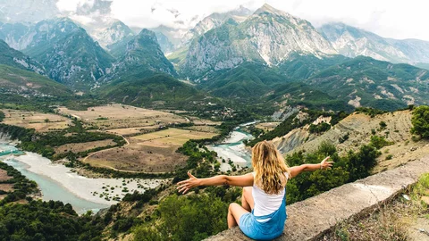 Ein Mädchen über dem Fluss Vjosa mit Bergkulisse im Hintergrund