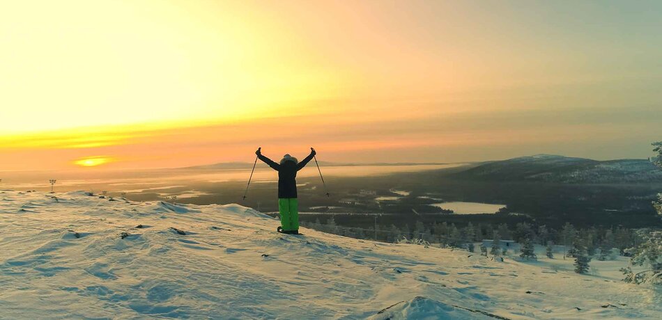 Eine Frau steht auf einer Erhöhung in Lappland vor den Sonnenuntergang