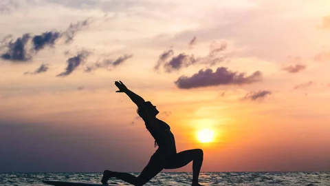 Frau beim SUP-Yoga beim Sonnenuntergang